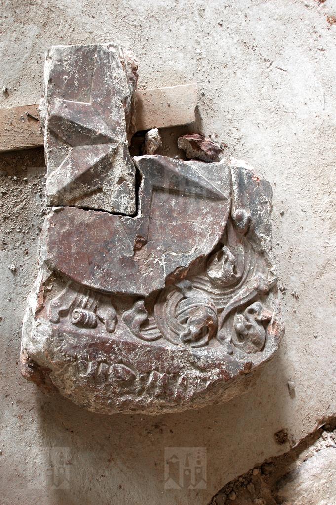 Časti nájdeného náhrobku s rodovým erbom a nečitateľným nápisom